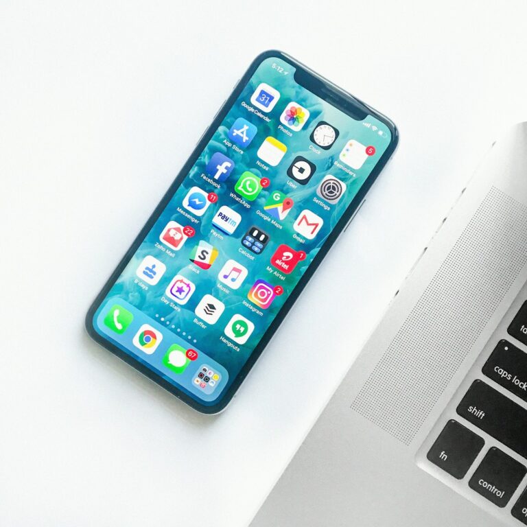 iPhone på ett vitt skrivbord bredvid en laptop